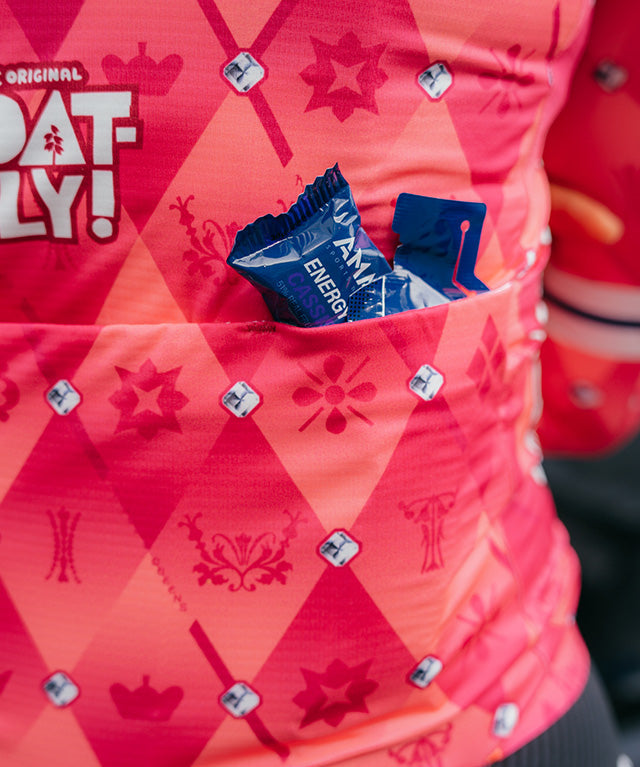Amacx Energy Fruit Chew Cassis in blue wrapper placed in the back pocket of a red patterned cycling jersey
