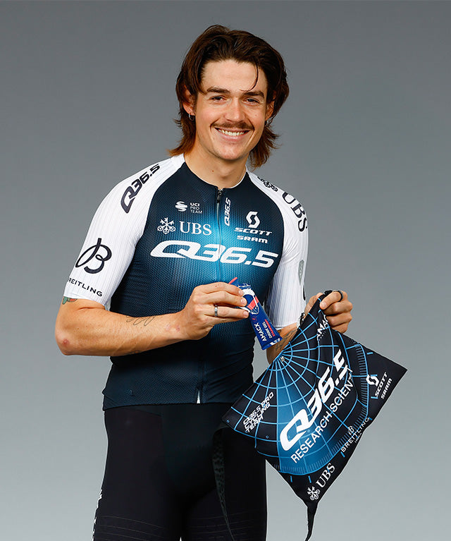 Smiling athlete in cycling gear holding Amacx Drink Gel Strawberry and a branded black and blue bag.