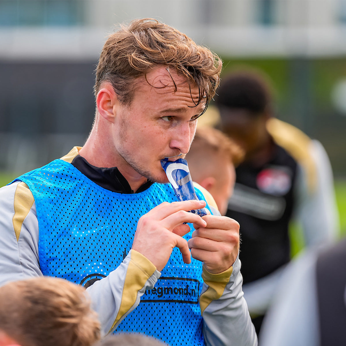 Man in sportswear consuming Amacx Drink Gel Cola Caffeine during outdoor training session on a blurred background
