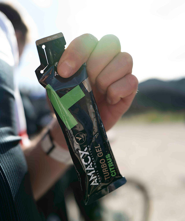 Hand holding a single-use pack of Turbo Gel Citrus energy gel outdoors with blurred background.