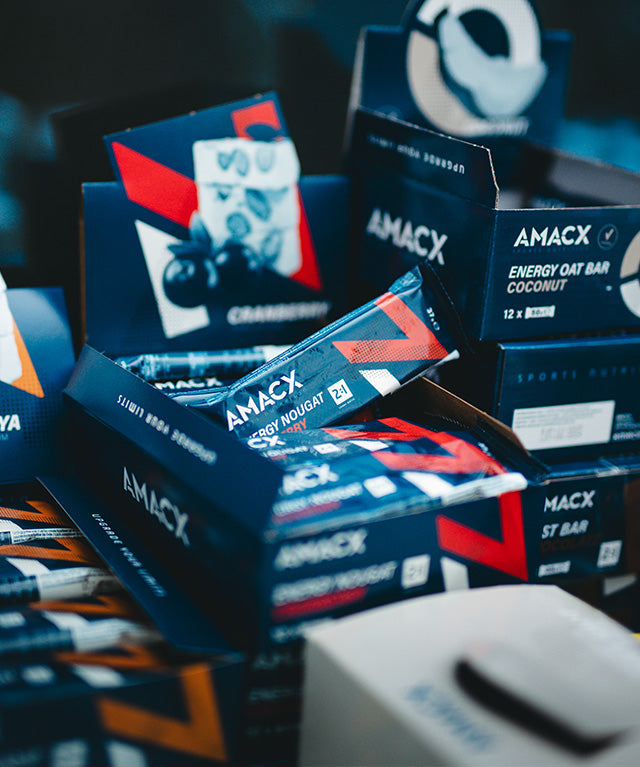 Close-up of Amacx Energy Nougat Cranberry bars in branded blue and red packaging stacked in display boxes