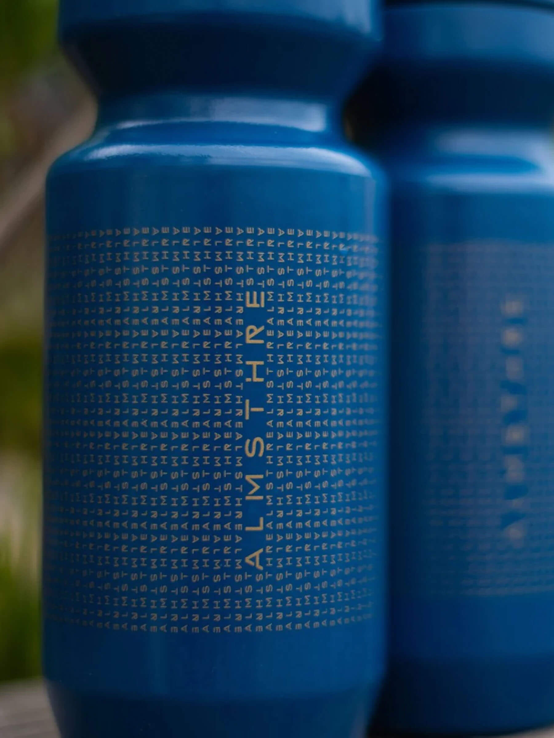 Close-up of blue ALMSTHRE Water Bottle with repeated logo text and MoFlo 2.0 Cap design details visible