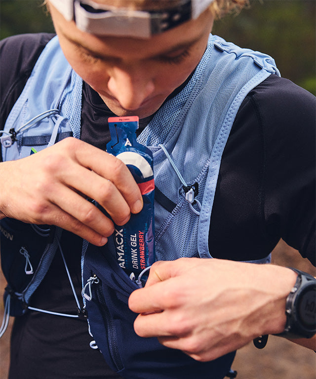 Runner taking out Amacx Drink Gel Strawberry from a blue hydration vest pocket during outdoor exercise
