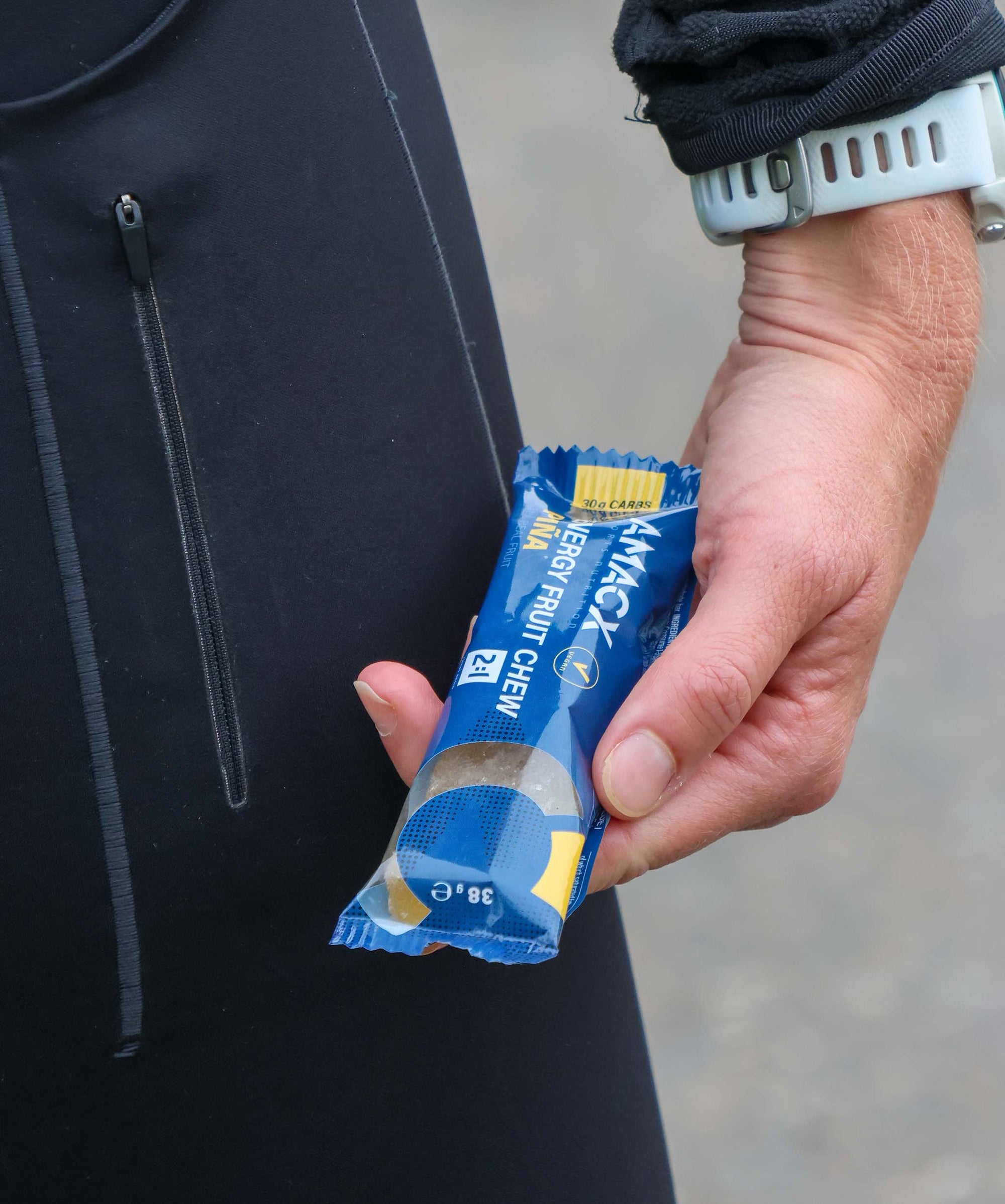 Hand holding a blue-wrapped Amacx Energy Fruit Chew Piña with a black sleeve and white watch visible on wrist