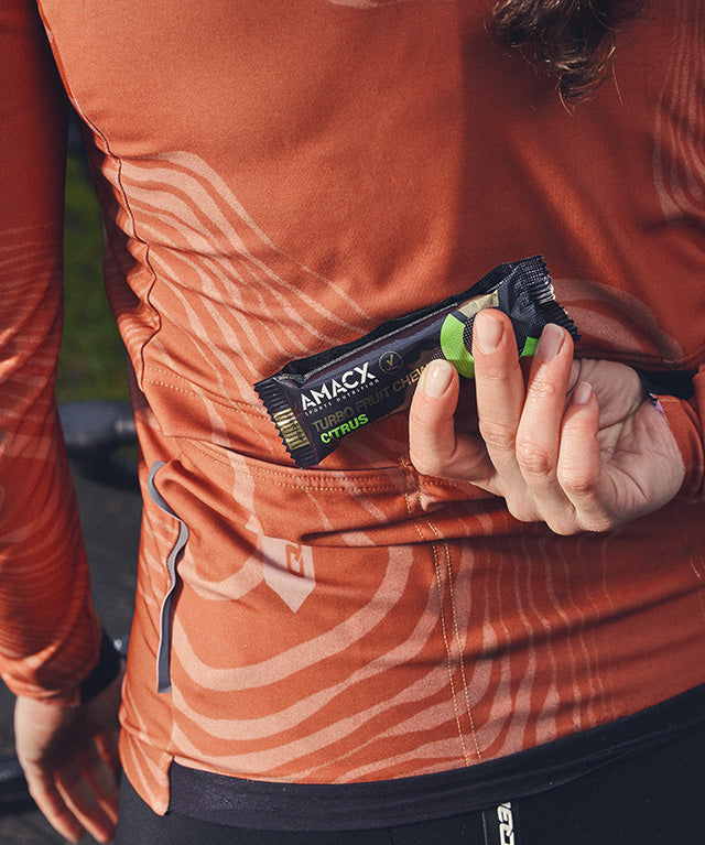 Person in athletic wear placing Amacx Turbo Fruit Chew Citrus energy bar into a back pocket while outdoors
