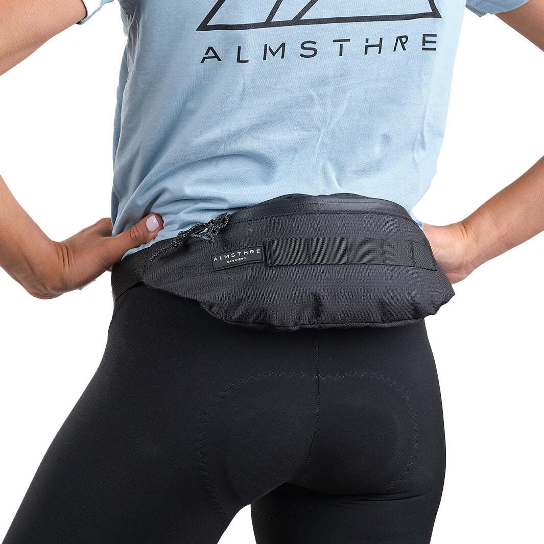 Person wearing ALMSTHRE Fanny Pack at waist with sleek black design and adjustable strap against white background