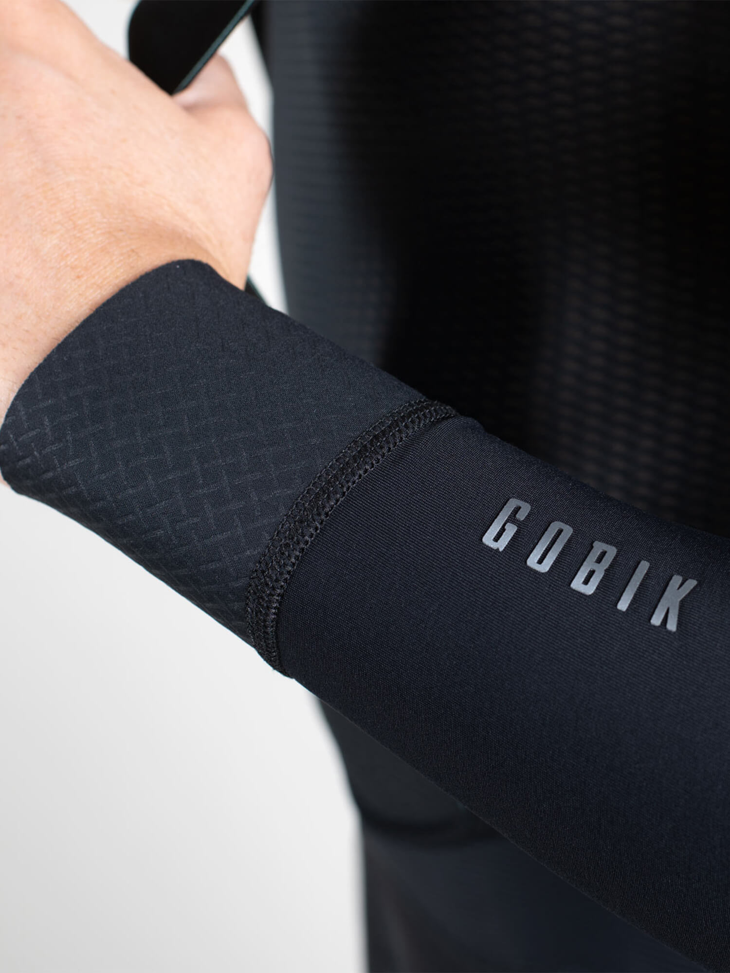 Close-up of unisex black GOBIK Kaba 2.0 Pitch thermal arm warmers on cyclist’s arm with textured fabric wrist cuff