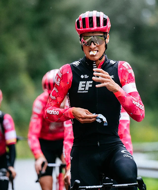 Athlete in red cycling gear eating Energy Nougat Papaya | 12 pack energy bar during a group ride outdoors in portrait view