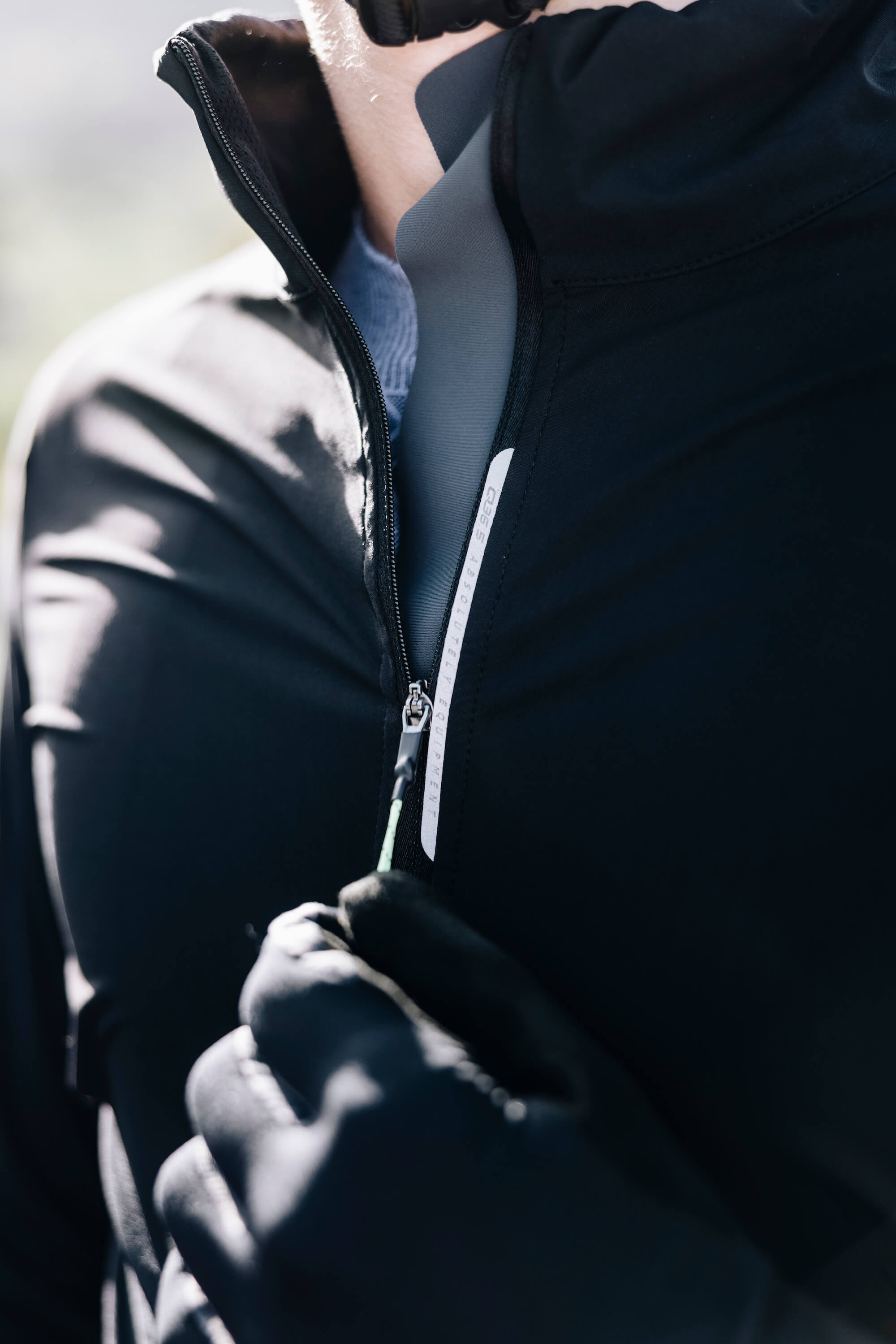 A cyclist zipping up the black Q36.5 Bat Shell Jersey, emphasizing the weatherproof and moisture-preventing properties of the fabric.