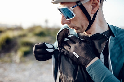 A cyclist adjusting the black Q36.5 Wind Shell over the shoulder, demonstrating its practicality and ease of use during outdoor activities.