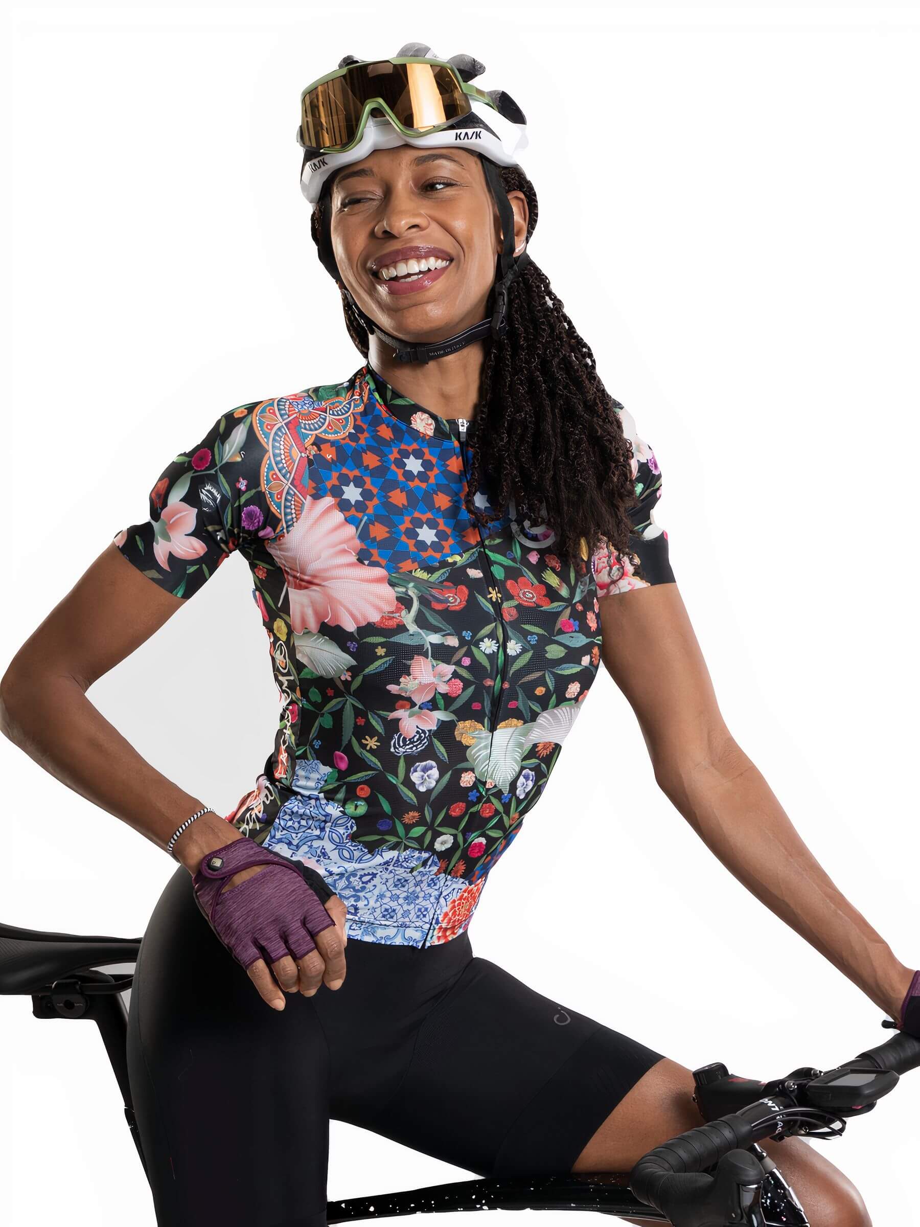 Woman wearing Ostroy Omloop Jersey - Women's floral cycling top and helmet while seated on a bike against white background