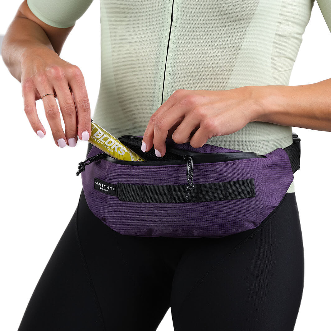 Close-up of person using purple ALMSTHRE Fanny Pack with adjustable strap and front zipper pocket against white background