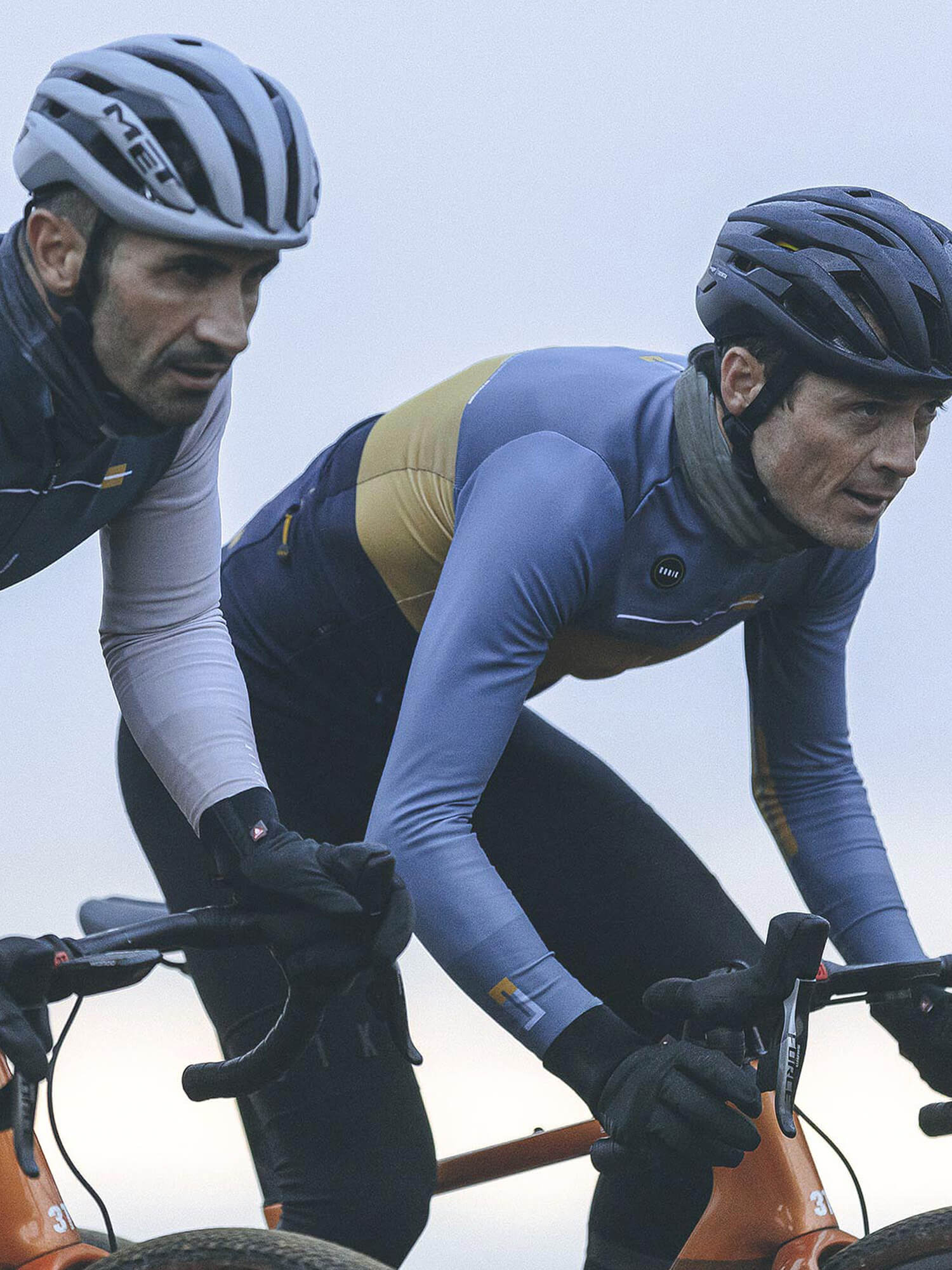 Two cyclists wearing helmets and GOBIK Moonbah Merino Neck Warmers during a cool weather ride outdoors